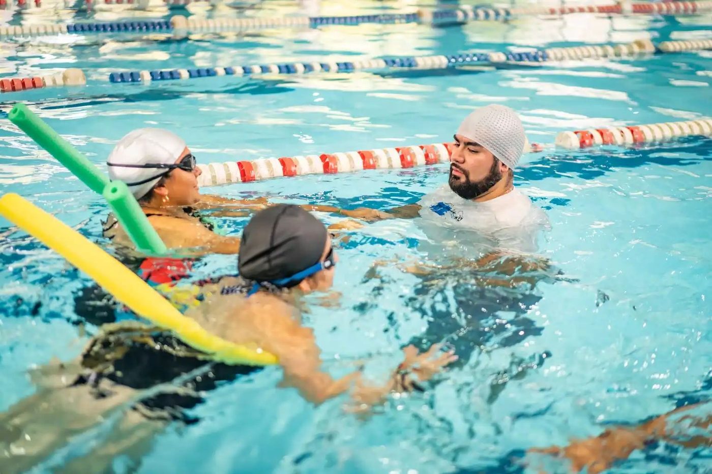 Instructor guiando a dos adultos en una clase de natación en la piscina temperada